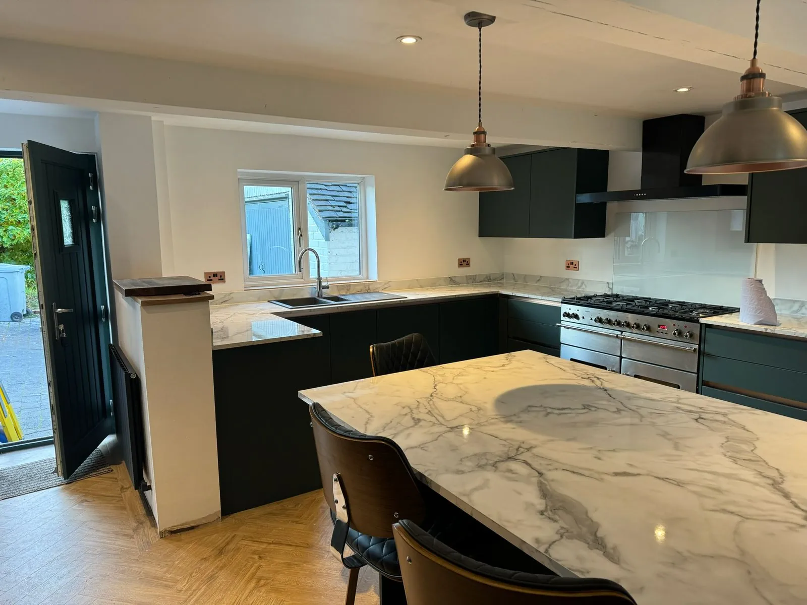 Full kitchen fit-out with dark green units, marble-effect island and herringbone floor by Warm-Wise